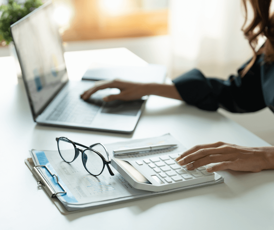 Personne utilisant un ordinateur portable et une calculatrice avec des documents financiers sur un bureau, représentant un cabinet comptable association